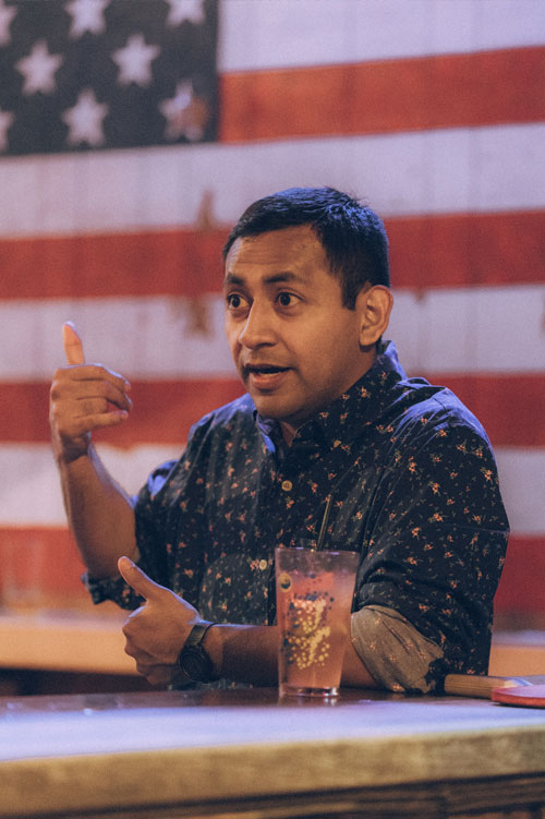 Cesar at a bar with a large American flag behind him